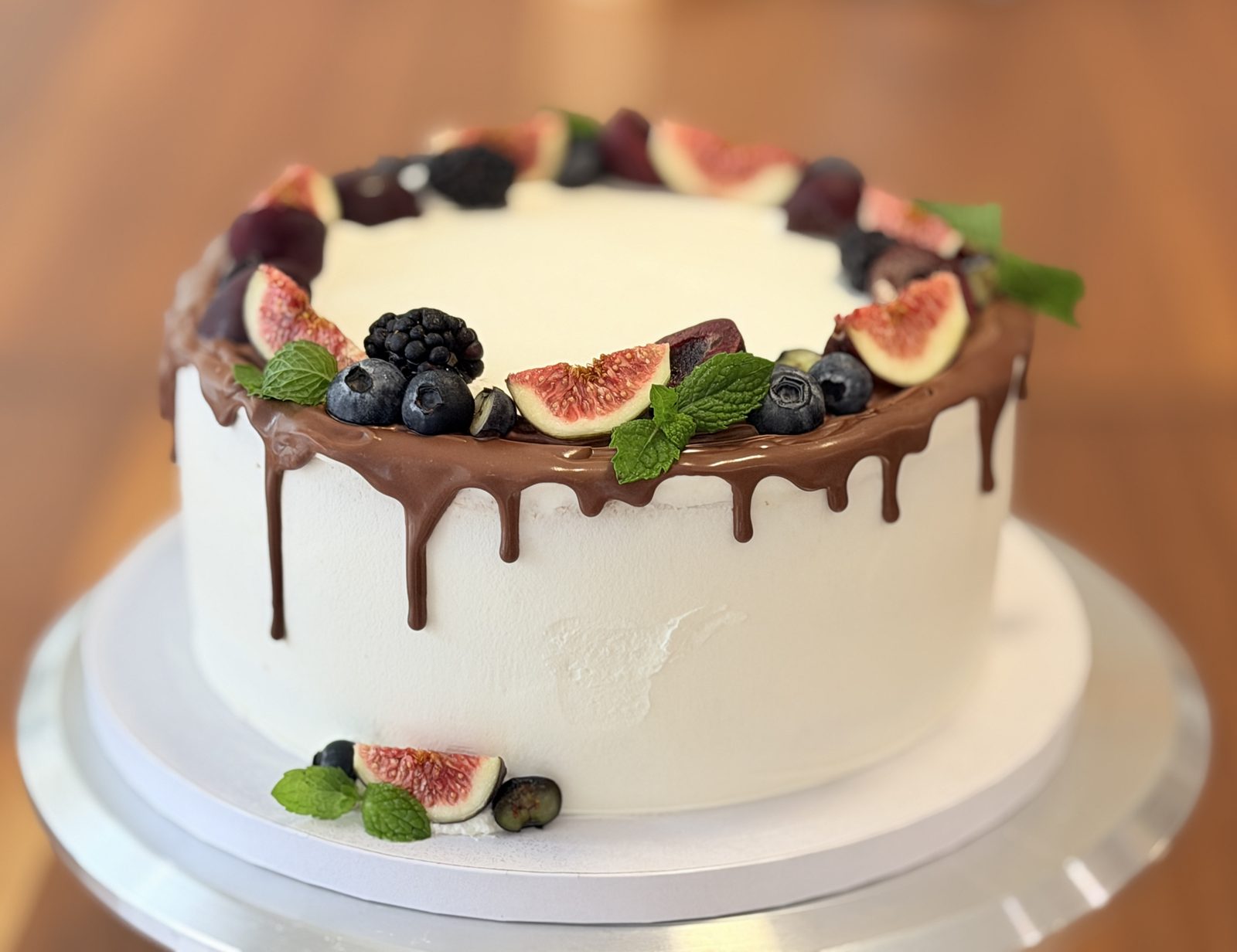 White buttercream cake with a chocolate ganache drip, topped with figs, blackberries, blueberries and mint