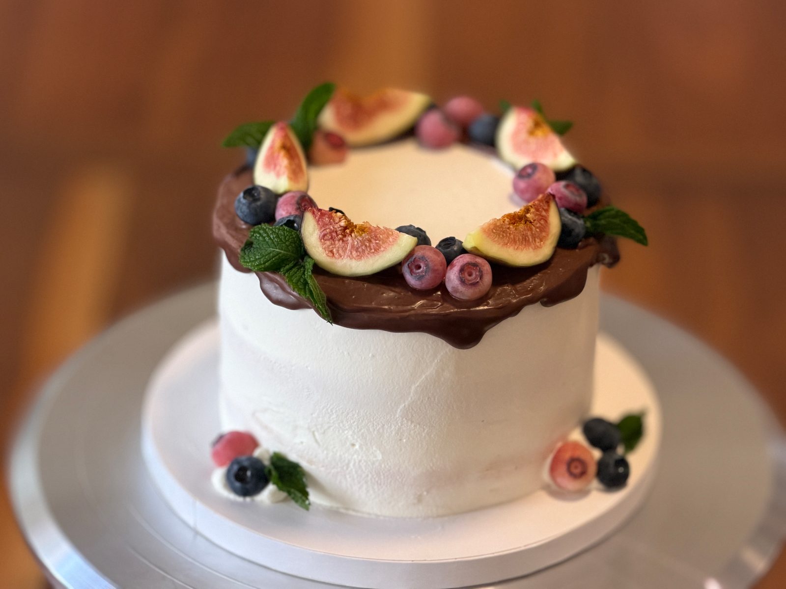 Overhead view of a cake with chocolate ganache, figs, blueberries and mint