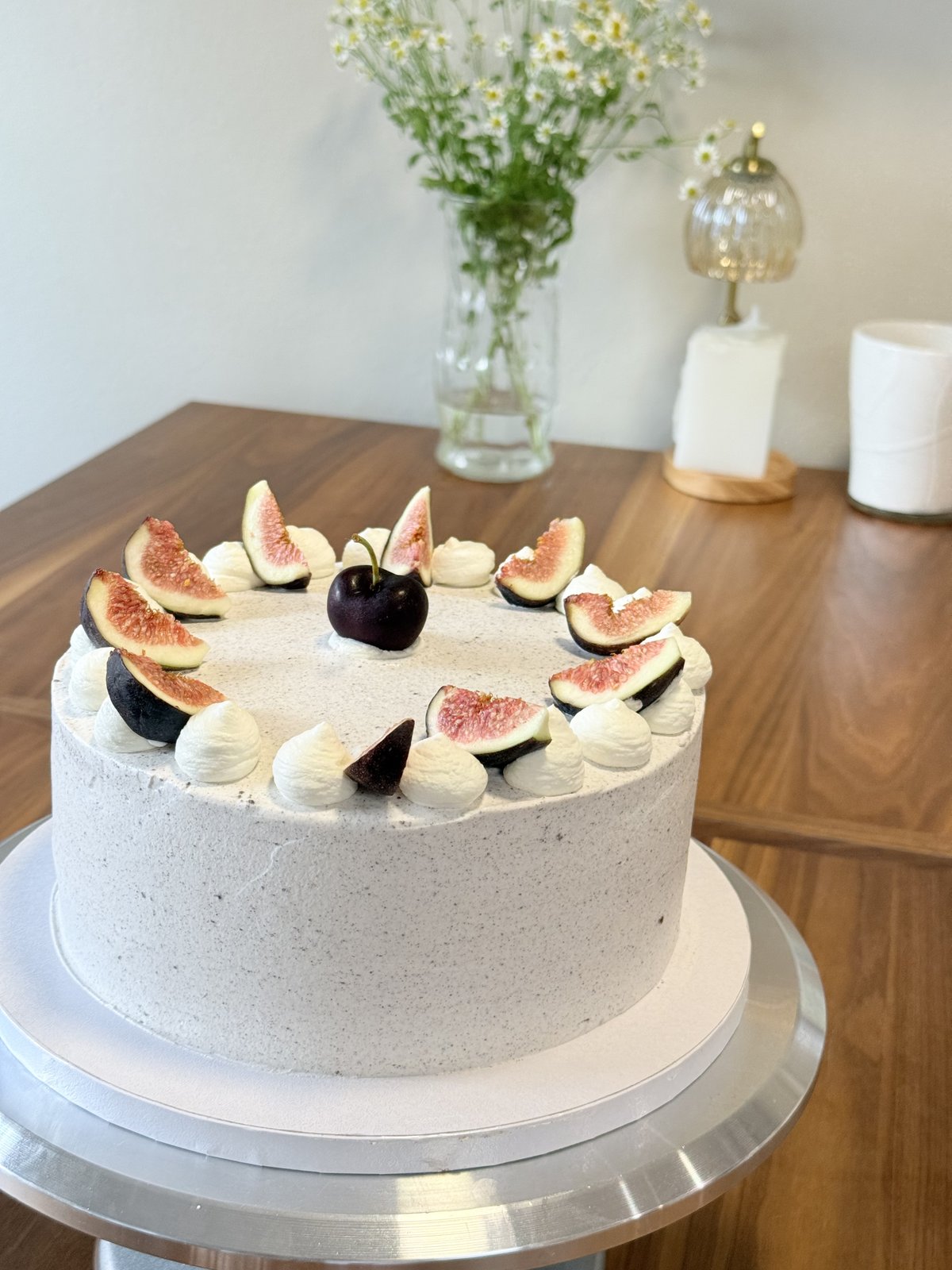 Fig and cherry cake styled on a wooden table with flowers in the background