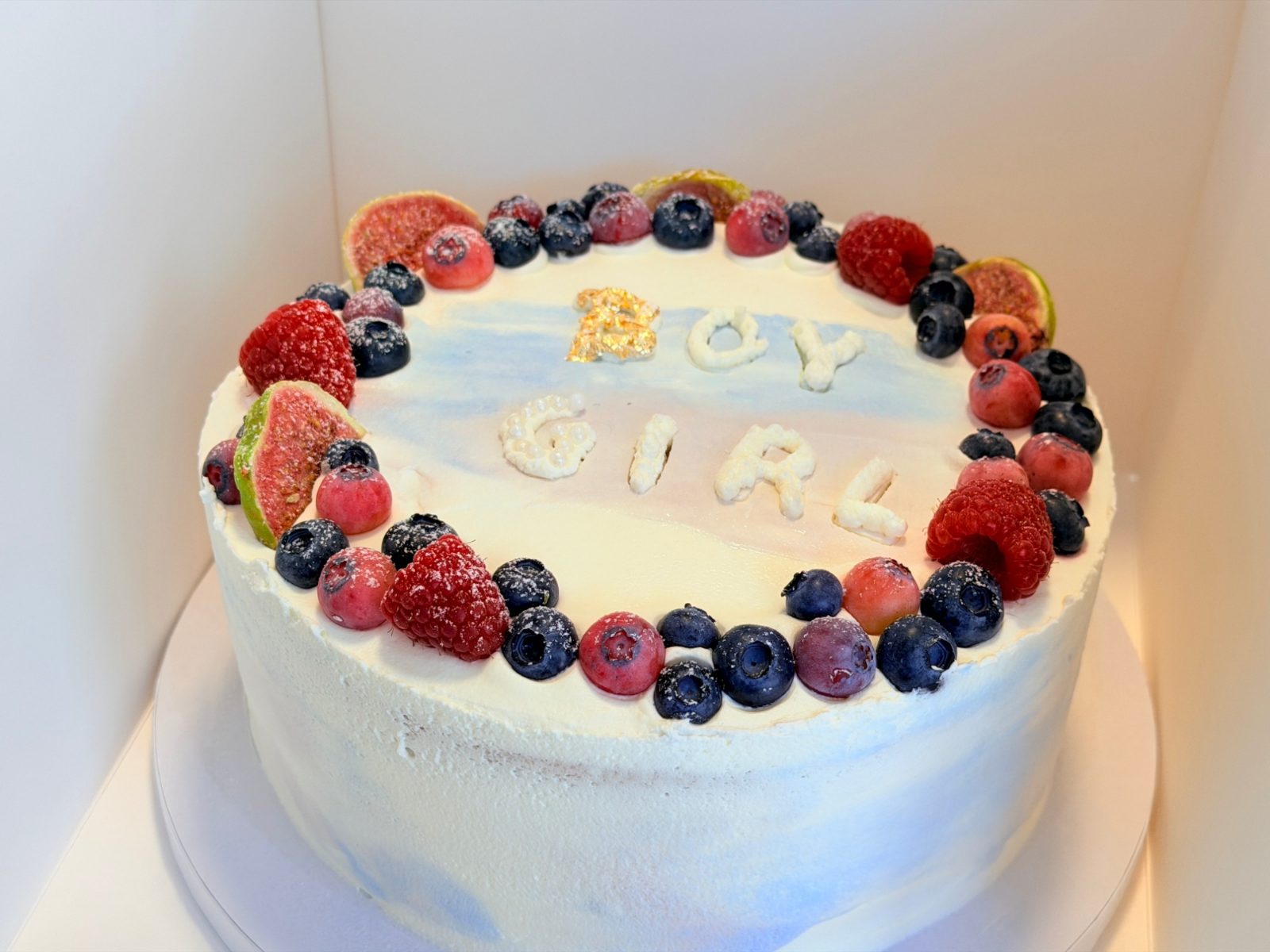 Gender-reveal cake with fresh berries and 'Boy or Girl' lettering
