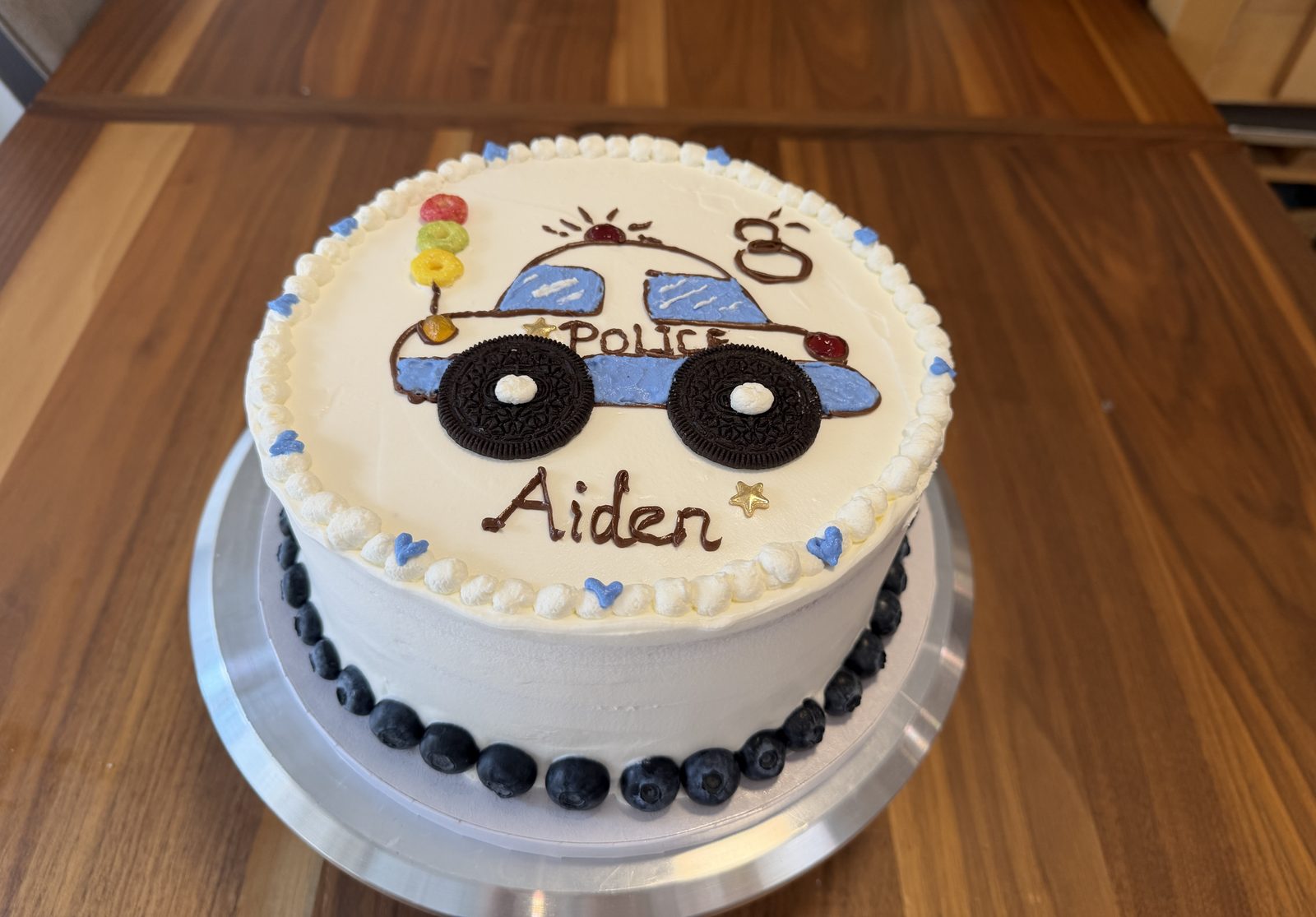 Kids' birthday cake hand-piped with a blue police car, Oreo wheels and a blueberry border