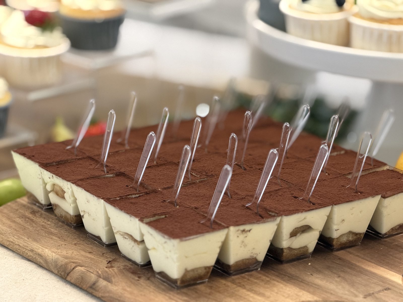 Tray of individual tiramisu cups dusted with cocoa, each with a small serving fork